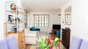 Uma sala de estar com sofá, mesa de centro com um vaso de flores, televisão e estante de livros.