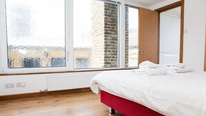 Quarto com uma janela grande, cama vermelha e radiador branco.