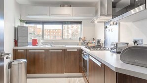 A modern kitchen with wooden cabinets, a stainless steel range hood, and a window providing a view of buildings outside. - Incredible, Modern Apartment in South Kensington (London)