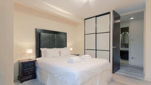 A neatly made bed with white linens and a headboard, a bedside table with a lamp, and a large sliding door leading to a bathroom. - Incredible, Modern Apartment in South Kensington (London)
