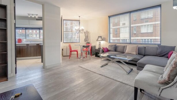 A modern living room with a grey sofa, a coffee table, and a dining area with red chairs. - Incredible, Modern Apartment in South Kensington (London)