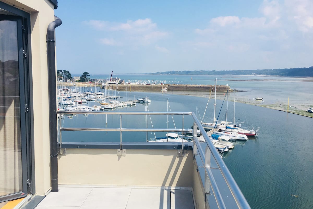 Un balcón con vista a una marina llena de barcos, una playa de arena y una costa lejana.