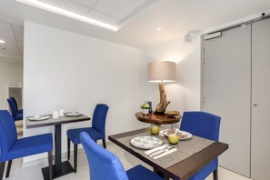 A dining area with a table set for two, blue chairs, a lamp, and a view of a door. - Le Nautica by Akena Hotels (Perros-Guirec)