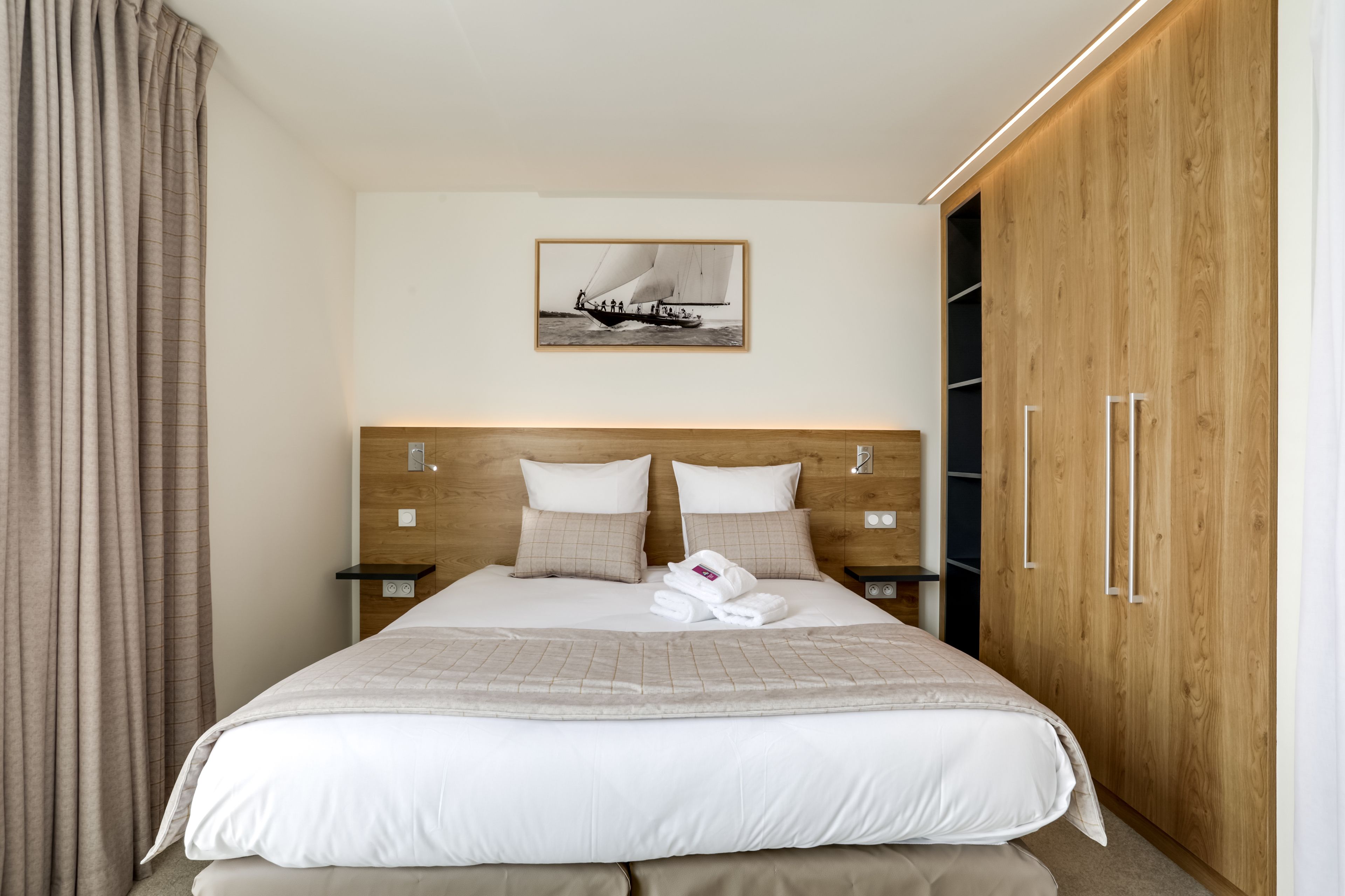 A neatly made bed with a headboard, a bedside table with a lamp, and a wooden wardrobe.