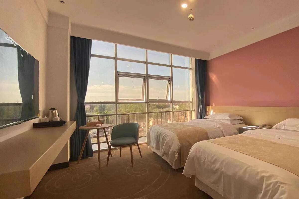 A hotel room with two beds, a desk, a chair, and a large window offering a view.