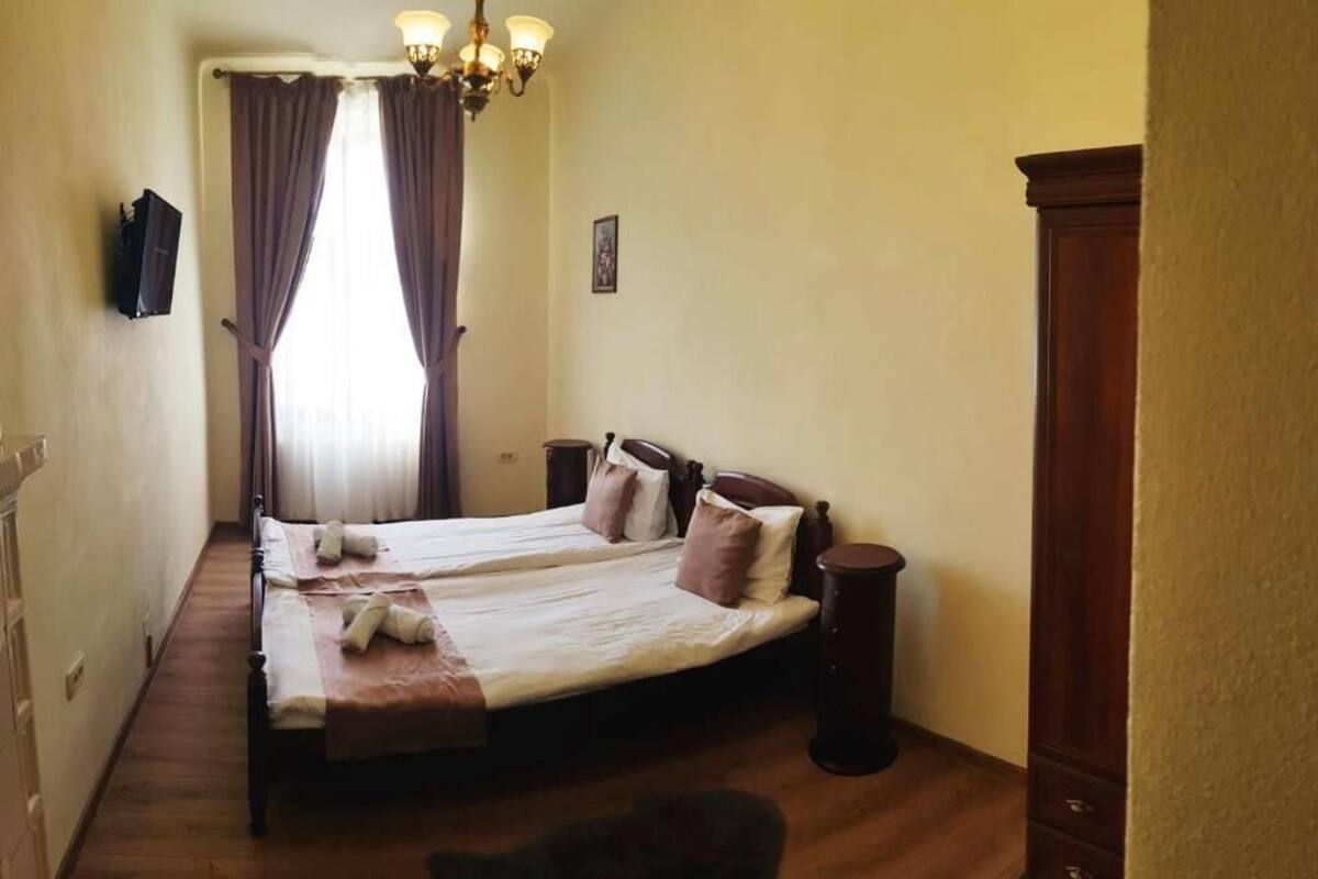 A bedroom with two beds, a wooden floor, a chandelier, and a wooden wardrobe.