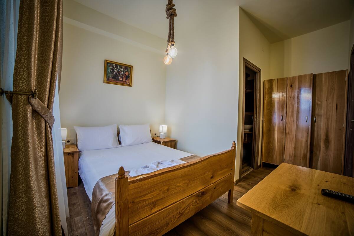 A wooden bed with a white mattress, a bedside table with a lamp, and a wooden wardrobe.