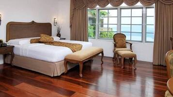 A hotel room with a large bed, a bench, two chairs, a nightstand, and a window with curtains.