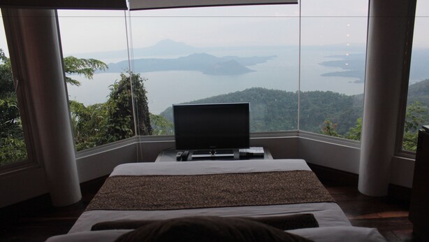 A bedroom with a large window overlooking a lake and mountains. - Villa Ibarra (Tagaytay)
