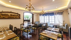 A dining area with wooden tables and chairs, chandeliers, and a large window with curtains. - Villa Ibarra (Tagaytay)