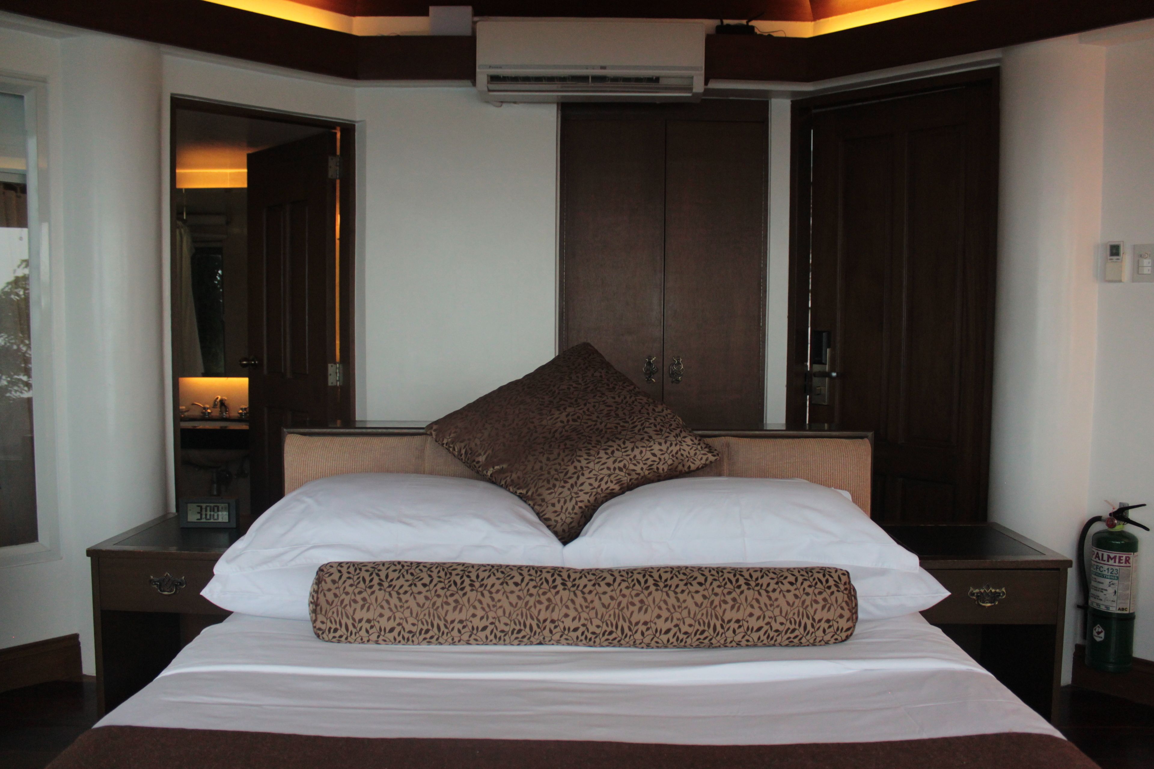 Una habitación de hotel con cama, mesita de noche, armario y equipo de aire acondicionado.