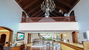 A spacious lobby with a wooden reception desk, a chandelier, and a staircase leading to an upper level. - Villa Ibarra (Tagaytay)
