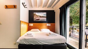 Habitación de hotel con cama, un cuadro colgado con una vista panorámica y una ventana que da al exterior.