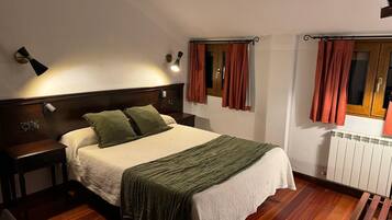 A bedroom with a bed, nightstands, a wooden bench, a radiator, and curtains.