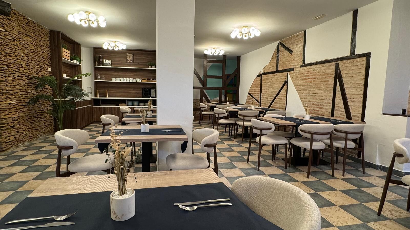 Un restaurante con suelo a cuadros, sillas modernas y una mesa central con un jarrón de plantas secas.