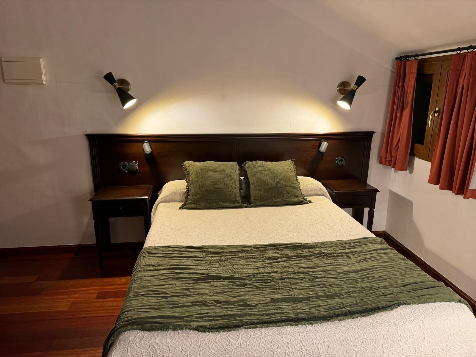 A neatly made bed with a green and white duvet, two bedside lamps, and a wooden headboard.