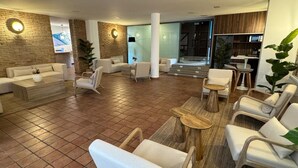 Een ruime lobby met diverse zitmogelijkheden, waaronder banken en stoelen, een salontafel en een klein houten tafeltje. Er staan potplanten en hangt een grote spiegel aan de muren.
