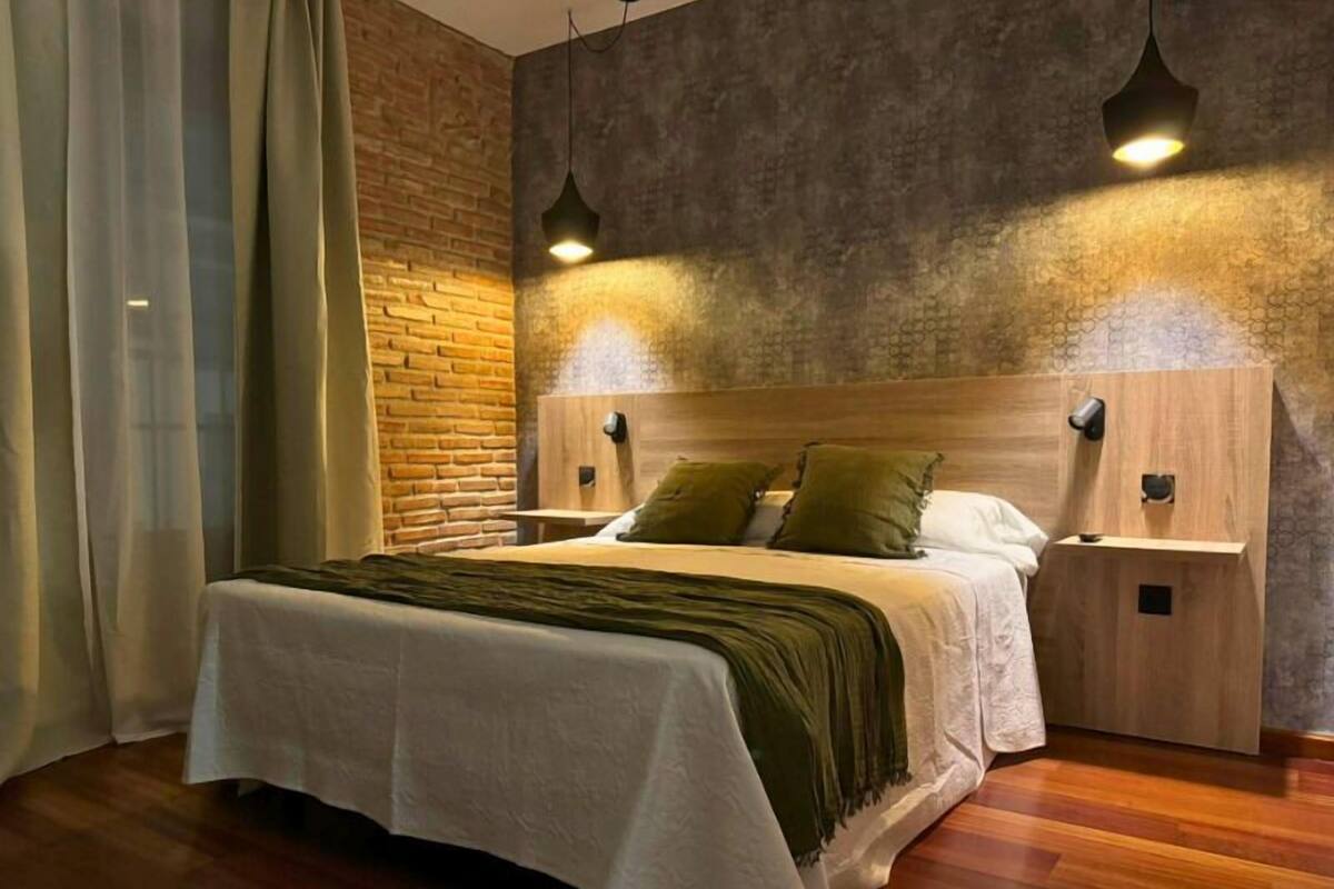 Een moderne slaapkamer met een houten hoofdbord, een groot bed met wit beddengoed, twee nachtkastjes en een accentmuur van baksteen.