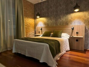 A modern bedroom with a wooden headboard, a large bed with white bedding, two bedside tables, and a brick accent wall. - Hotel La Fuente (Candelario)
