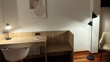 A modern, minimalist room with a wooden desk, a white chair, a floor lamp, and a wall-mounted artwork.
