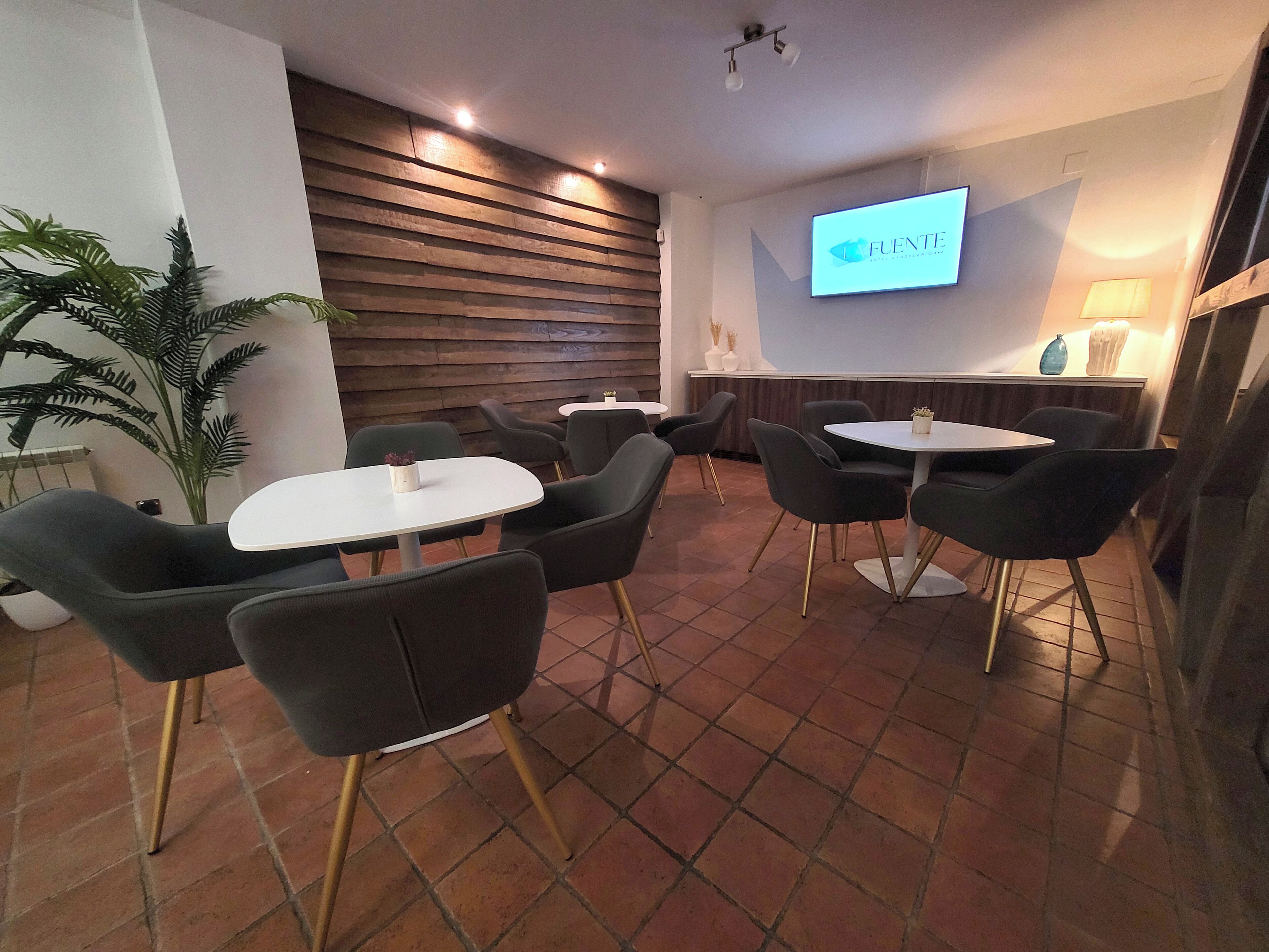 A modern lounge area with round tables and black chairs, a wooden slatted wall, and a TV screen displaying 'FUENTE'.