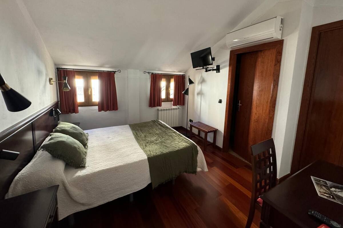 Een kleine, gezellige slaapkamer met een enkel bed, een bureau, een stoel en een aan de muur bevestigde televisie.