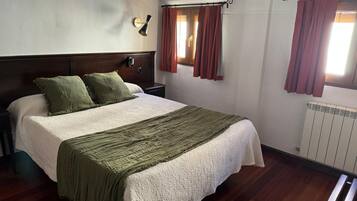 Un dormitorio con una cama grande, cabecera de madera, dos mesitas de noche, una lámpara de pared y una ventana con cortinas.