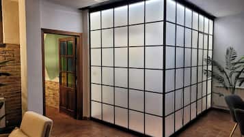 Una habitación con piso de baldosas, una puerta de madera, un amplio separador de vidrio esmerilado y una planta en maceta.