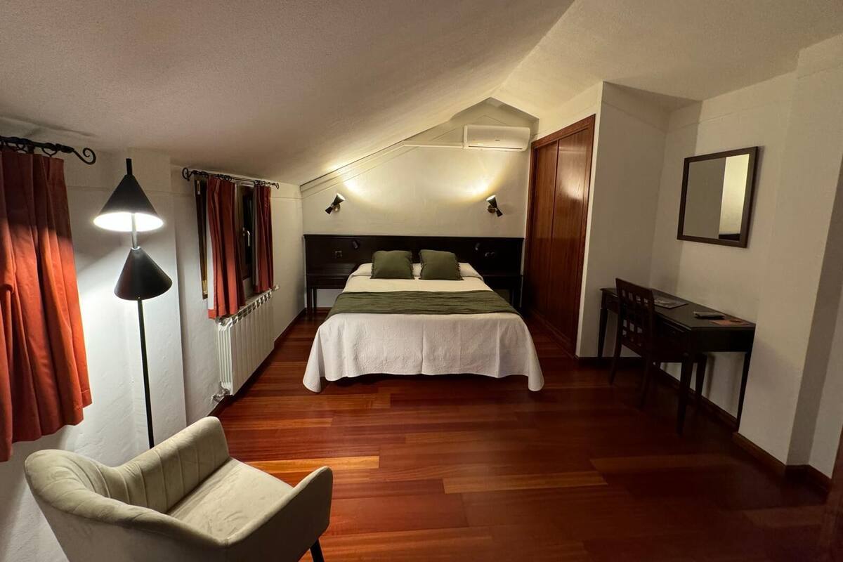Een slaapkamer met een bed, een bureau, een stoel, een lamp en een spiegel.