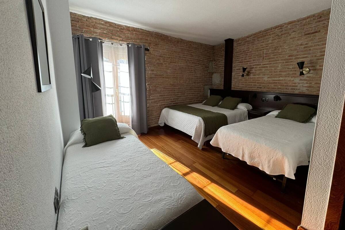 Een hotelkamer met twee bedden, een bakstenen muur, een raam met gordijnen en een nachtkastje met een lamp.
