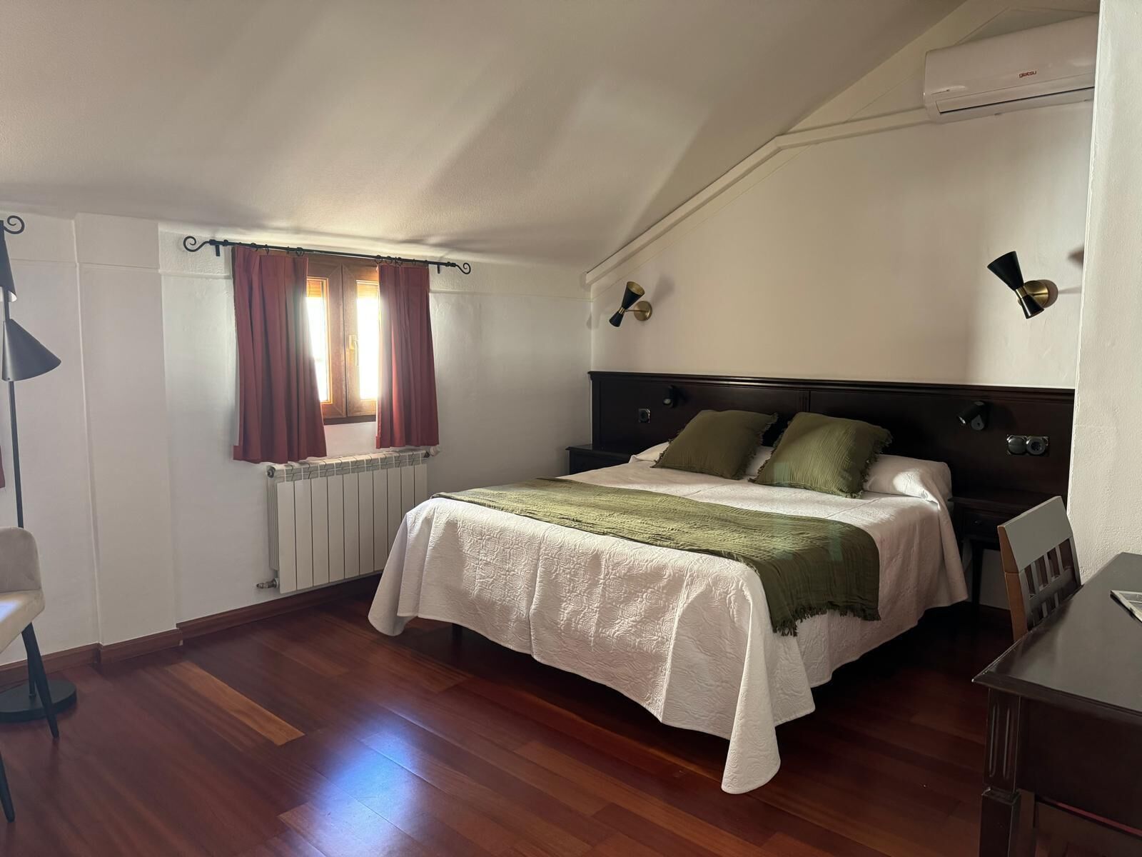Un dormitorio con cama, un radiador, una ventana con cortinas, un escritorio y una silla.