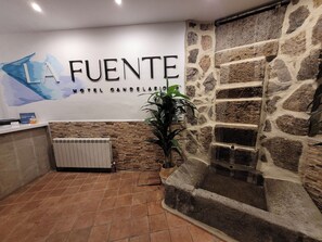 A reception area with a stone wall, a radiator, and a potted plant. - Hotel La Fuente (Candelario)