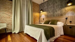 Een slaapkamer met een bakstenen muur, een bed met een houten hoofdbord, een stoel en een nachtkastje.