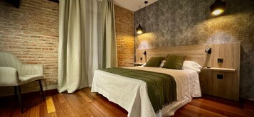 Un dormitorio con pared de ladrillo, una cama con cabecera de madera, una silla y una mesita de noche.