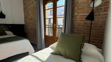 Ein Hotelzimmer mit Backsteinwand, einem großen Fenster mit Vorhängen, einem Bett mit weißer Bettwäsche und einer schwarzen Stehlampe.