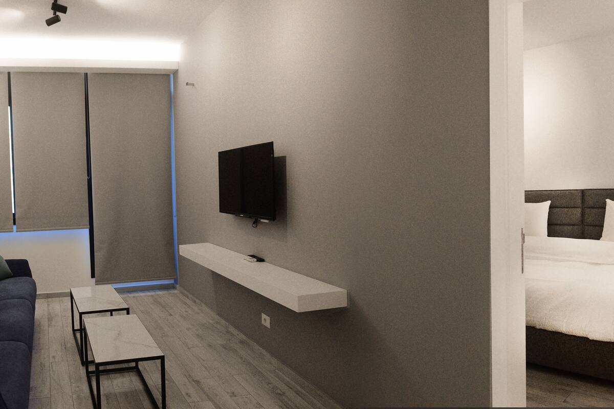 A modern hotel room with a sofa, a TV mounted on the wall, a bed with a headboard, and a small table.