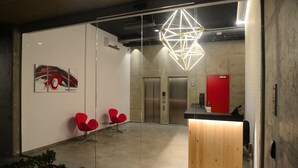 An office reception area with a glass wall, a wooden reception desk, red chairs, and a geometric light fixture. - 41 Twelve (Beirut)