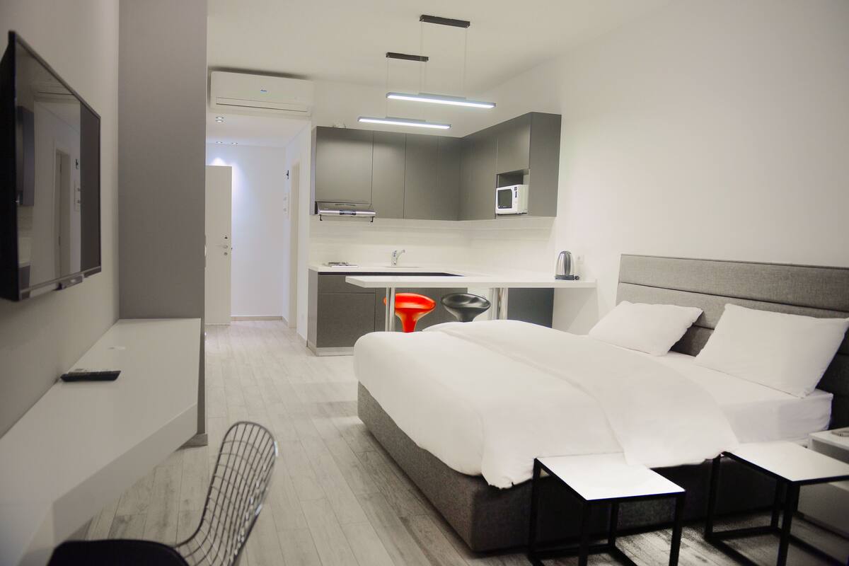 A modern hotel room with a large bed, a desk with a microwave, and a chair.