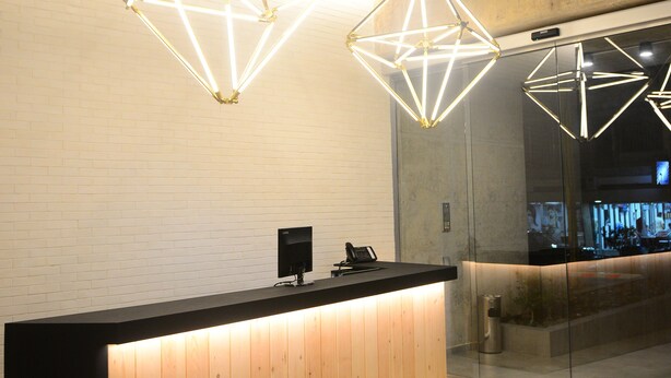 A reception desk with geometric pendant lighting, a wooden panel design, and a glass partition. - 41 Twelve (Beirut)