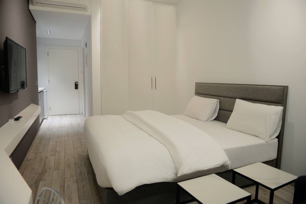 A hotel room with a bed, bedside tables, a TV, and a wardrobe.
