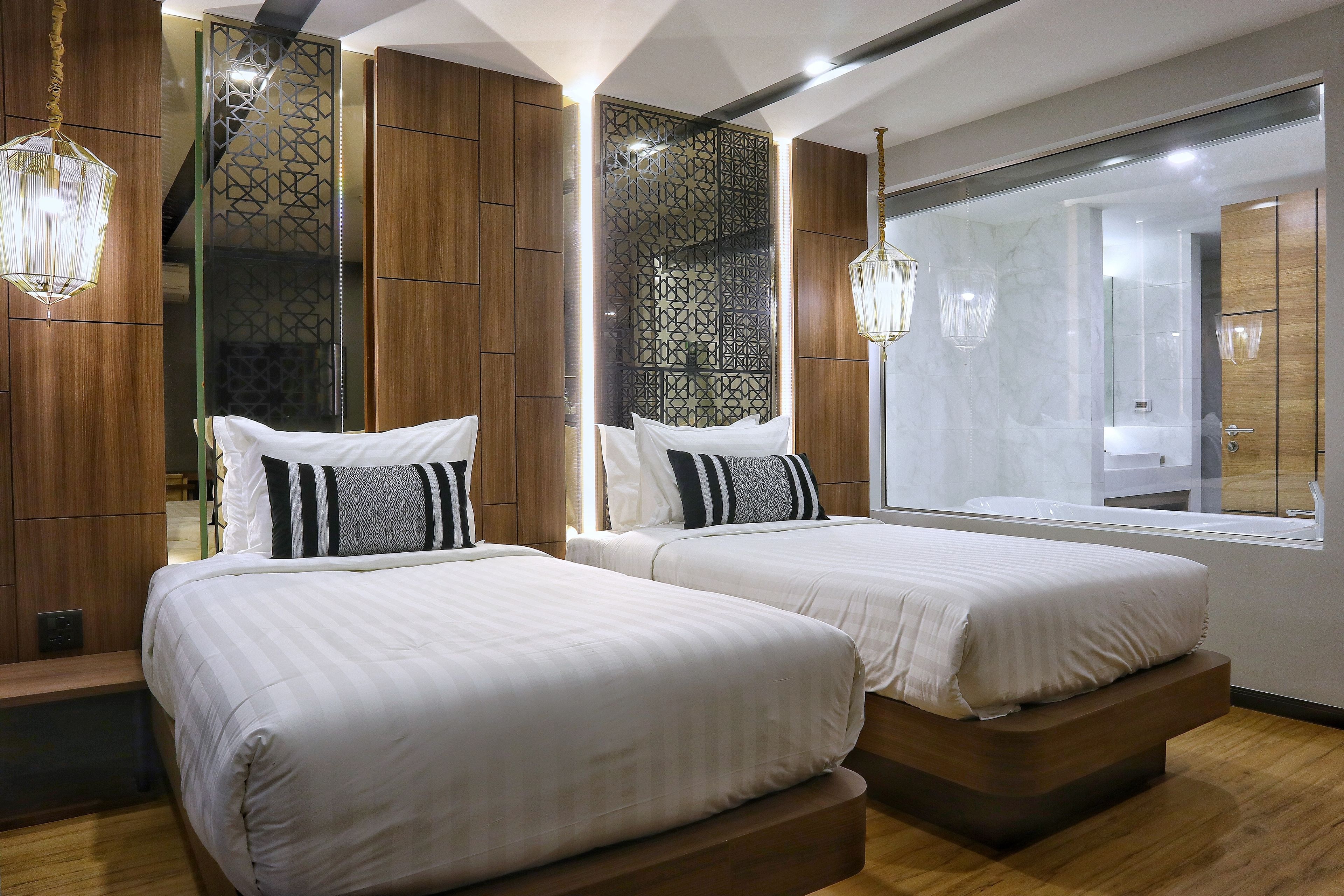 A modern hotel room with two beds, wooden paneling, a large mirror, and a view of the bathroom.