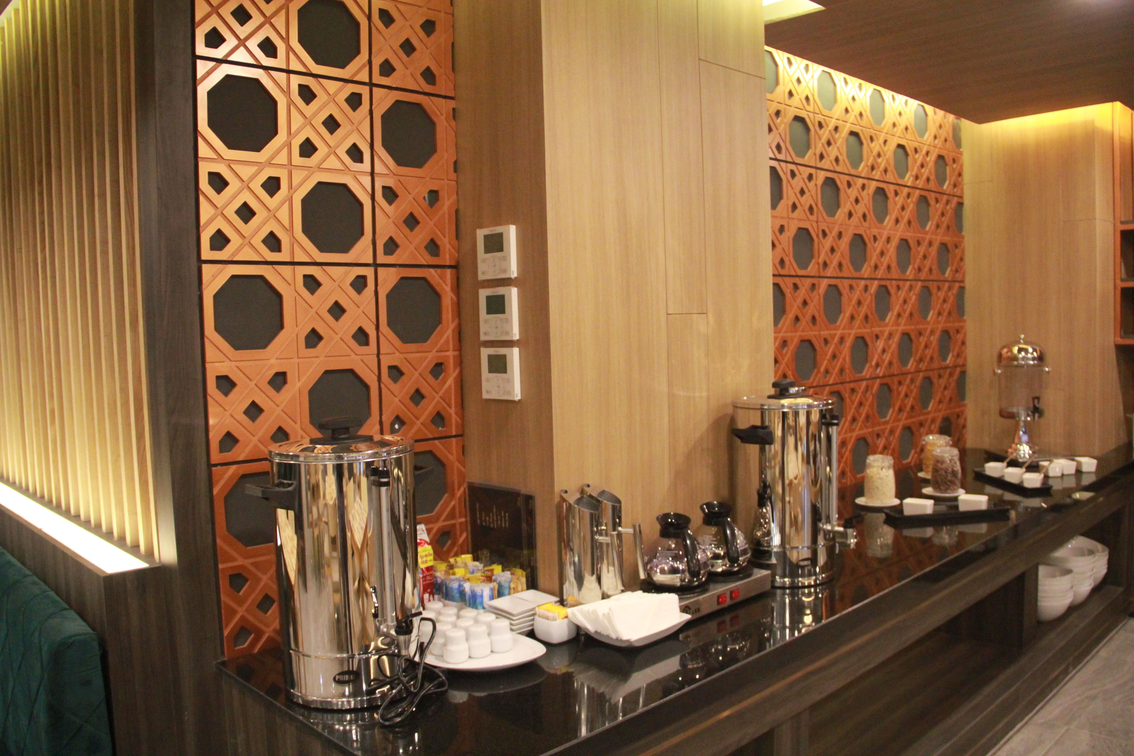 A hotel reception area with a coffee station, a mirror, and a decorative wall with geometric patterns.