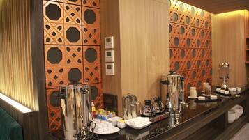 A hotel reception area with a coffee station, a mirror, and a decorative wall with geometric patterns.