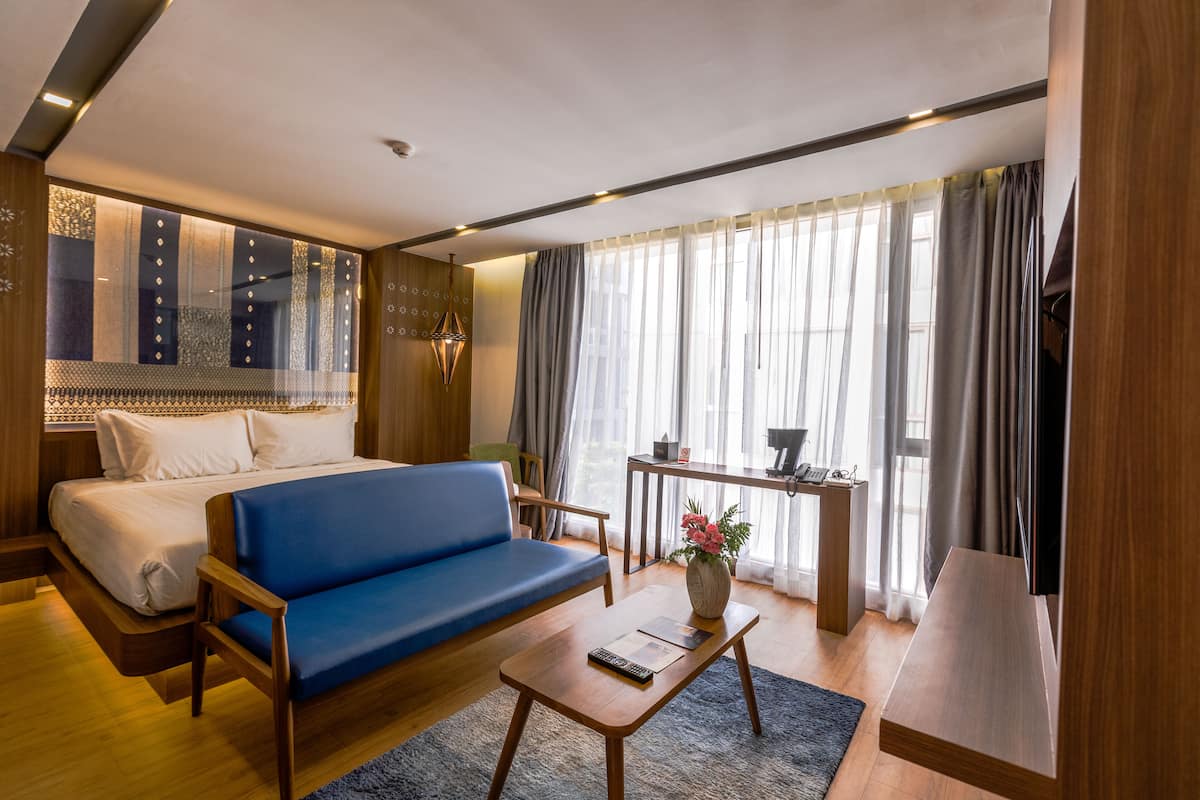 A modern hotel room with a bed, blue sofa, wooden coffee table, and a desk with a lamp.