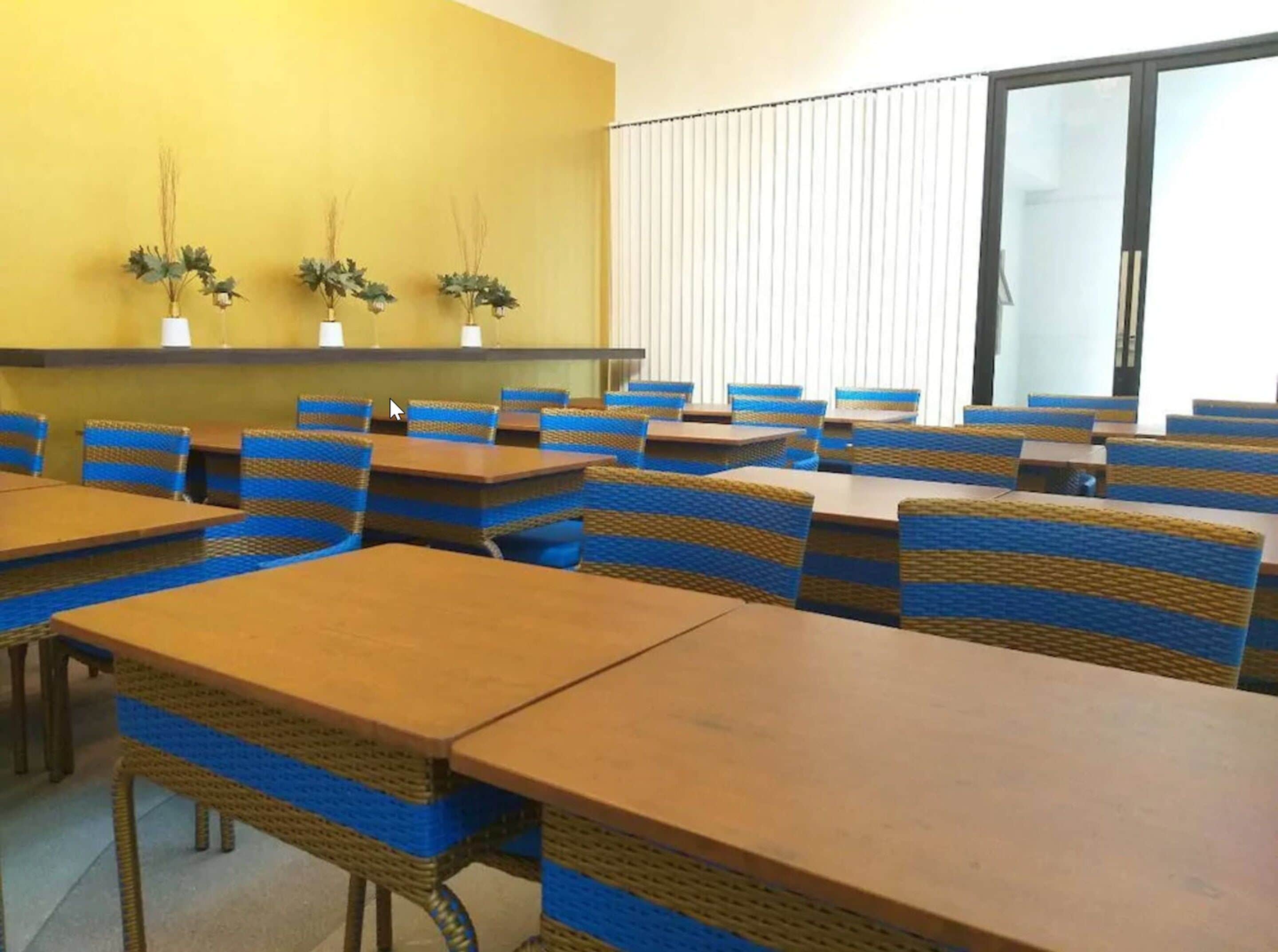 A conference room with tables and chairs, a yellow wall, and a window with blinds.