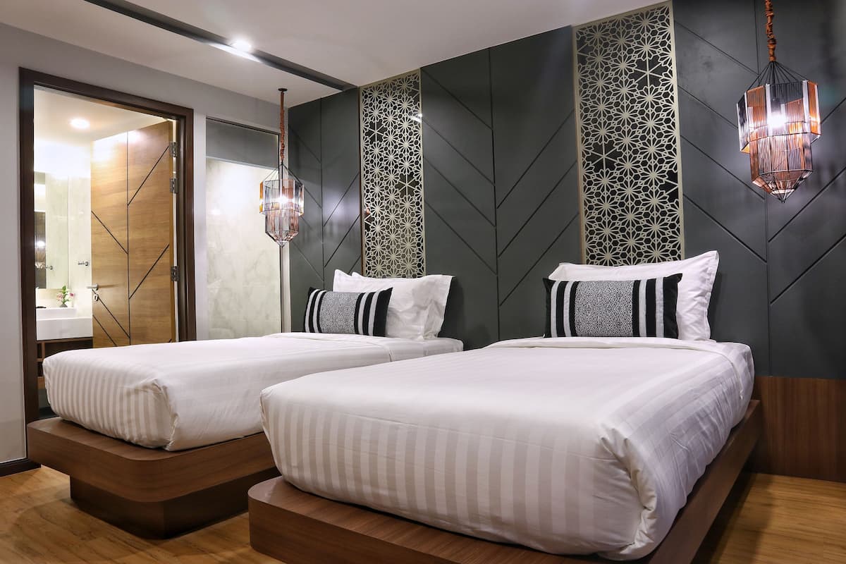 A modern hotel room with two beds, a large mirror, and decorative wall panels.