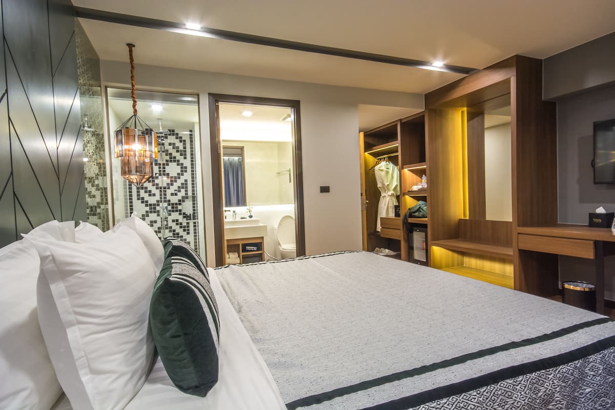 A modern hotel room with a large bed, a walk-in closet, a bathroom with a mirror, and a hanging light fixture.