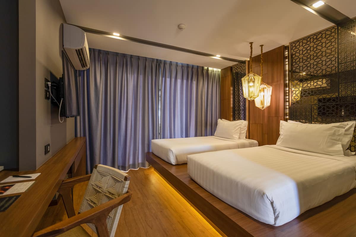 A hotel room with two beds, a desk with a chair, a TV, and a large window with curtains.