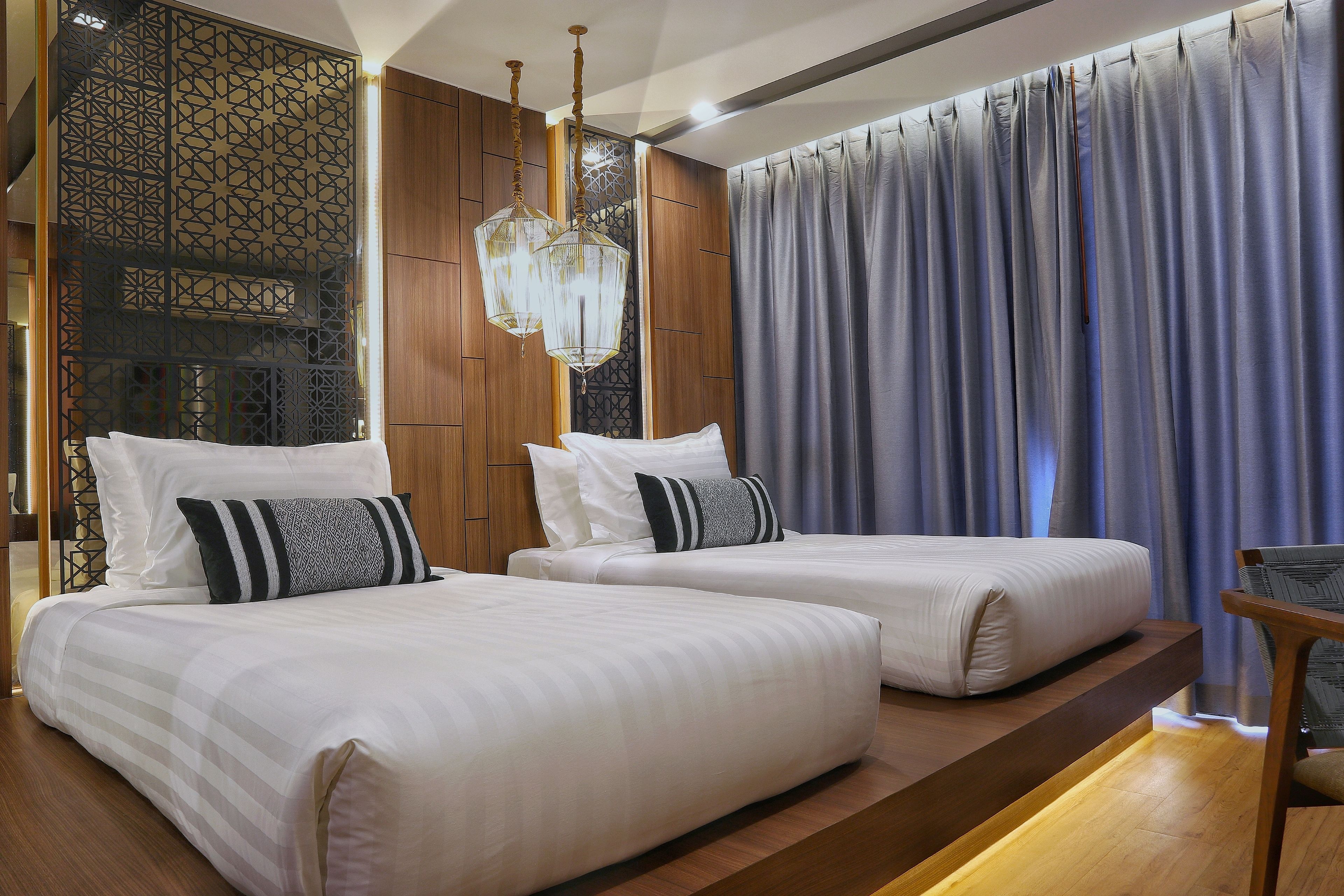 Habitación de hotel con dos camas, piso de madera, un detalle decorativo en la pared y un ventanal con cortinas.