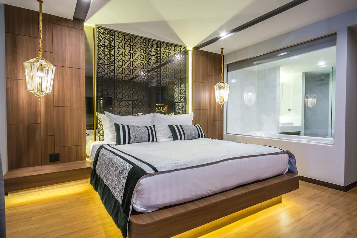 A modern bedroom with a large bed, wooden paneling, a decorative wall, and a large window.